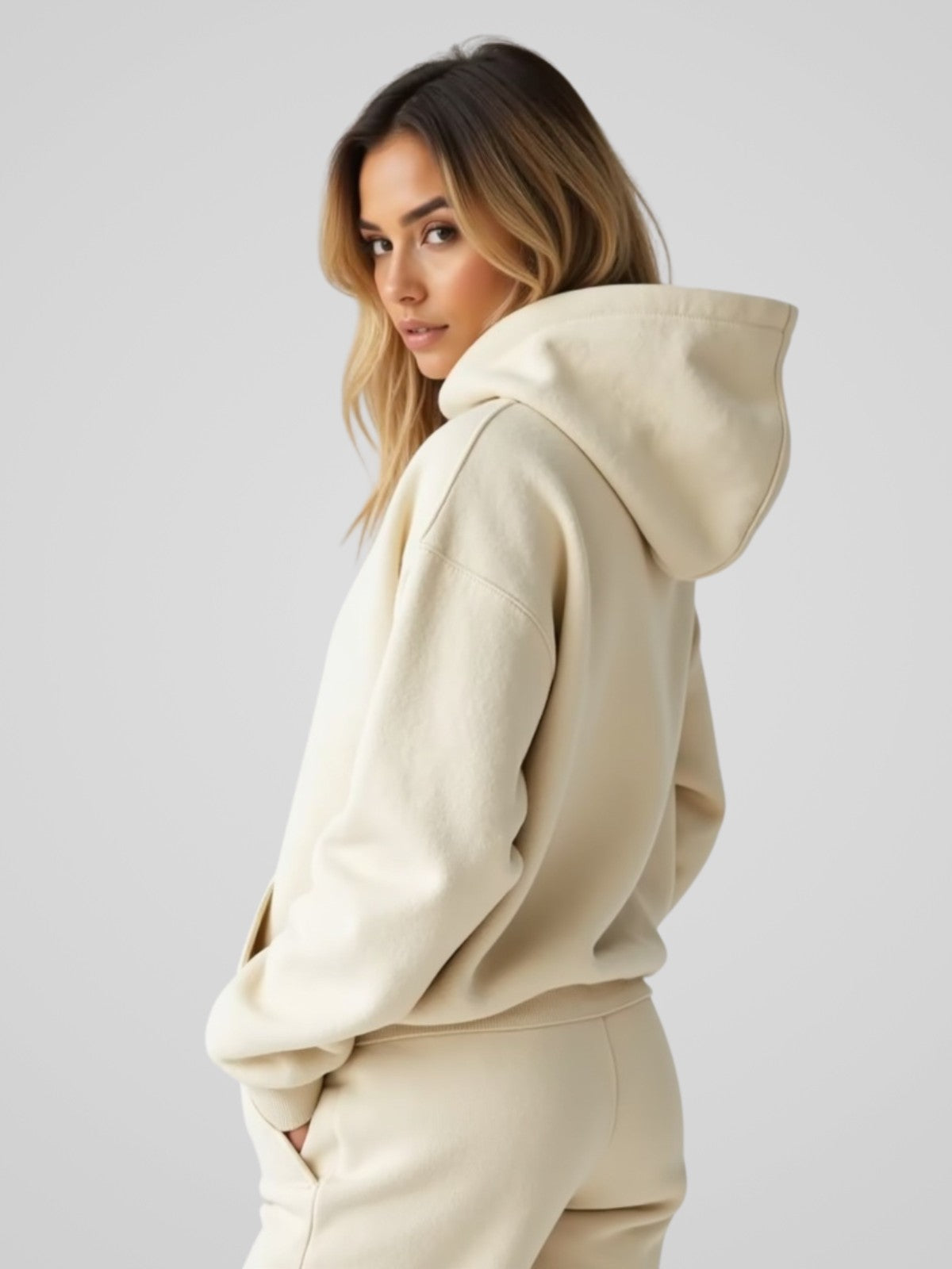 Woman wearing a cream oversized hoodie, standing backward and facing forward to show the fit and style.